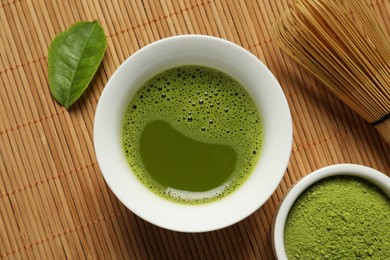 Cup of fresh matcha tea, green powder and chasen on bamboo mat, flat lay