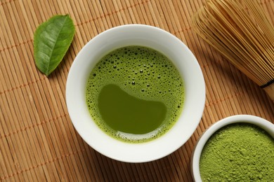 Photo of Cup of fresh matcha tea, green powder and chasen on bamboo mat, flat lay