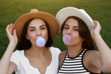 Photo of Beautiful women in hats blowing gums on green grass outdoors