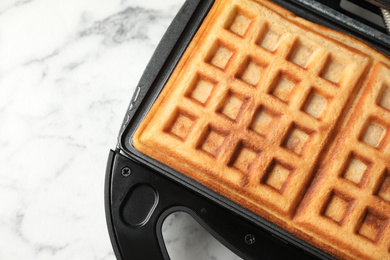 Photo of Modern iron with tasty Belgian waffles on white marble table, top view