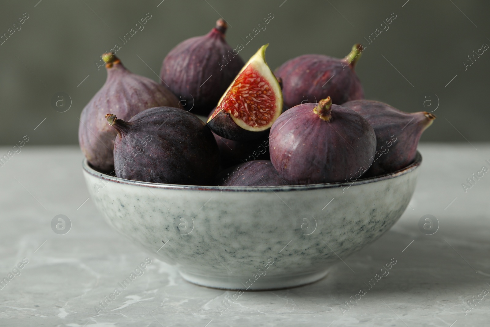 Photo of Tasty raw figs in bowl on light grey marble table, closeup