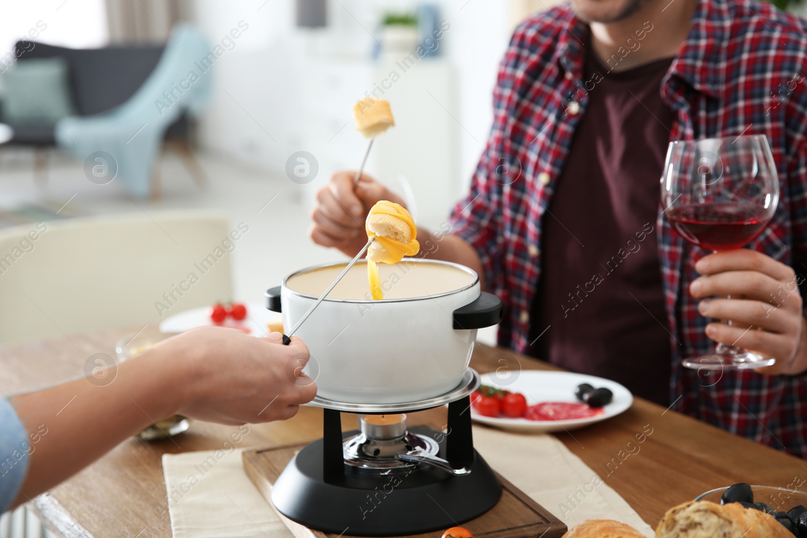 Photo of Couple having fondue dinner at table indoors, closeup