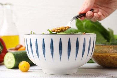 Woman pouring tasty vinegar based sauce (Vinaigrette) from spoon into bowl with salad at wooden rustic table, closeup