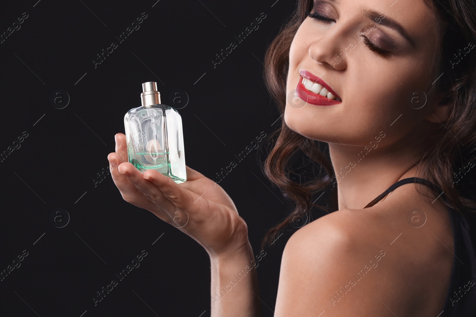 Photo of Beautiful young woman with bottle of perfume on black background