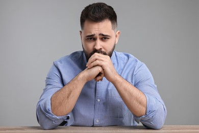 Photo of Portrait of sad man at wooden table on light grey background