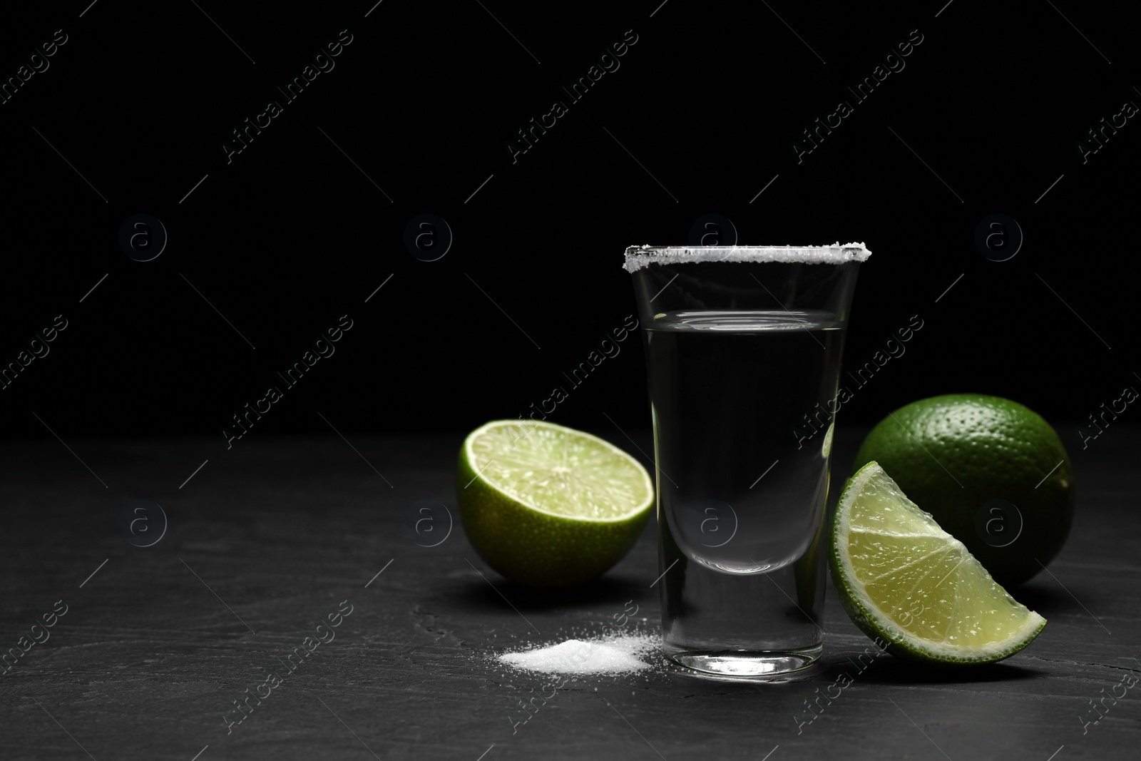 Photo of Mexican Tequila shot with salt and lime on black table. Space for text