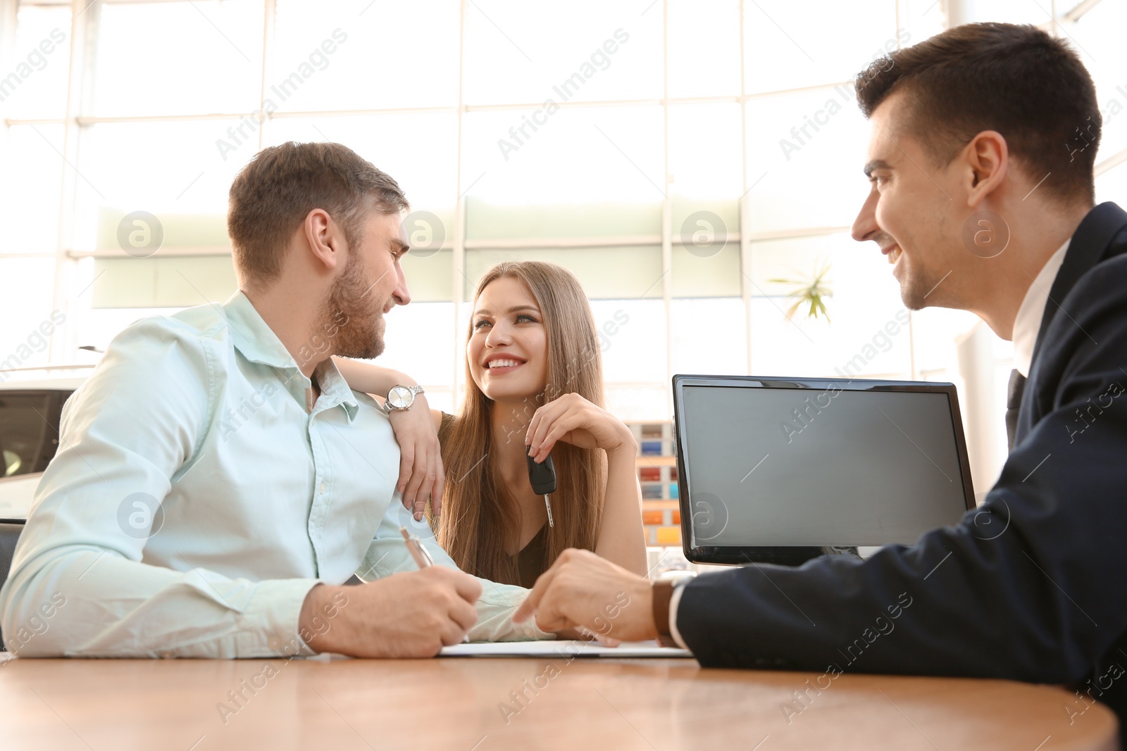 Photo of Young couple and salesman sitting at table in car salon. Buying auto