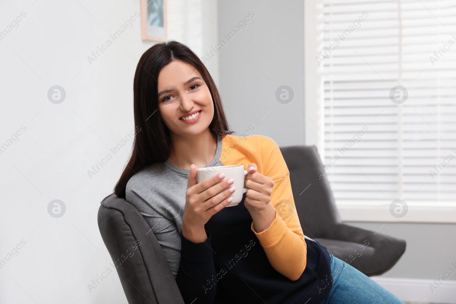 Photo of Young woman with cup of drink relaxing at home