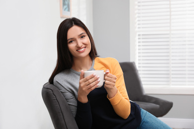 Photo of Young woman with cup of drink relaxing at home