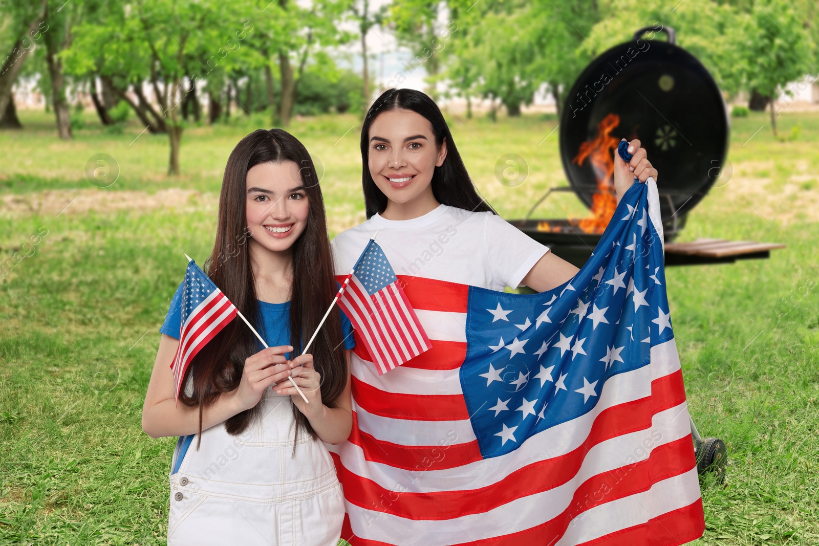 Image of 4th of July - Independence day of America. Happy mother and daughter with national flags of United States having picnic in park
