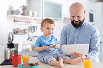 Photo of Dad and his little son using devices during breakfast in kitchen