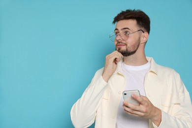 Handsome man in white jacket and eyeglasses with phone on light blue background, space for text