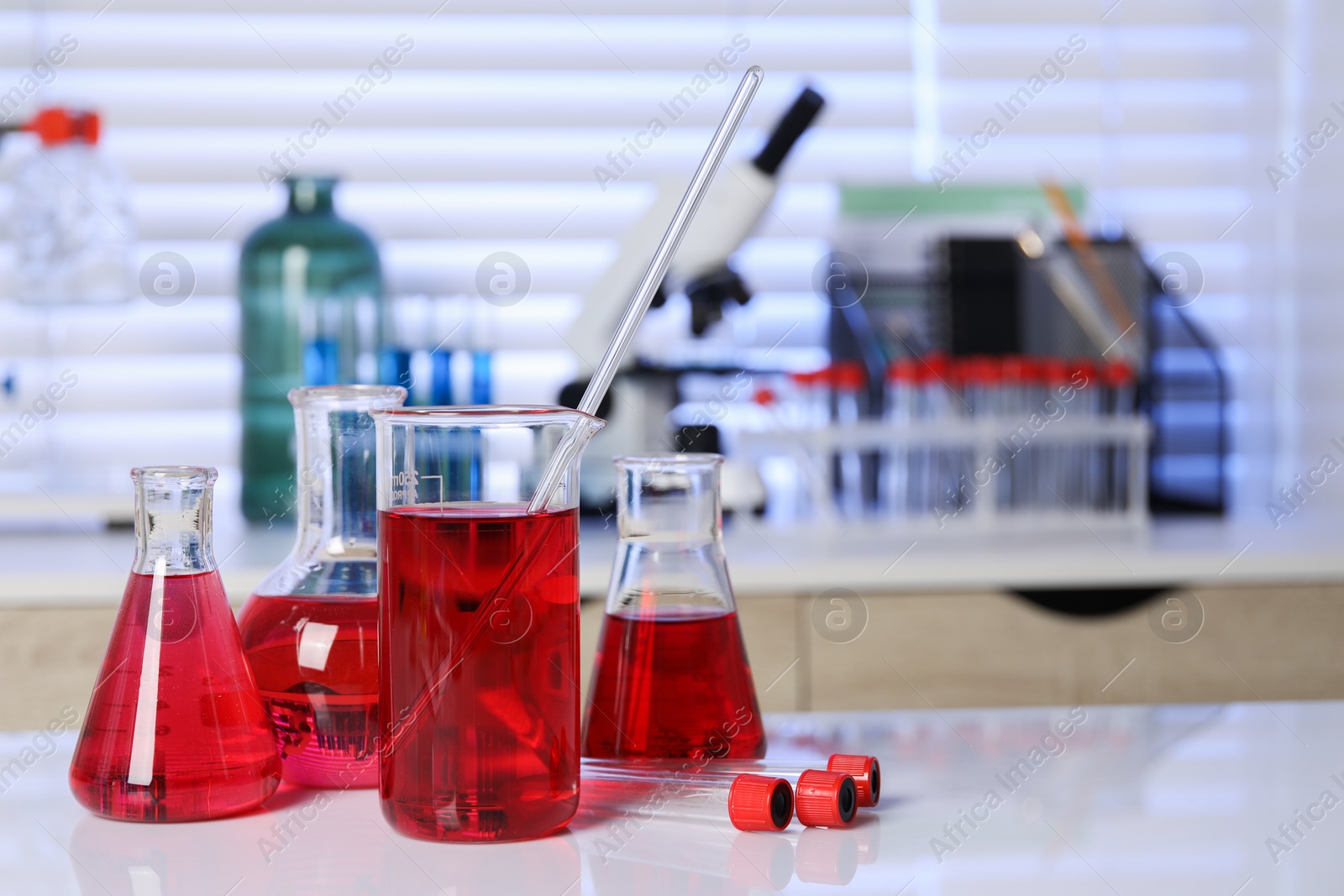 Photo of Laboratory analysis. Different glassware with red liquid on white table indoors. Space for text