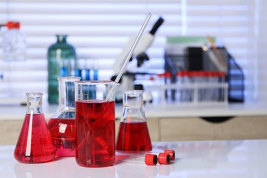 Laboratory analysis. Different glassware with red liquid on white table indoors. Space for text