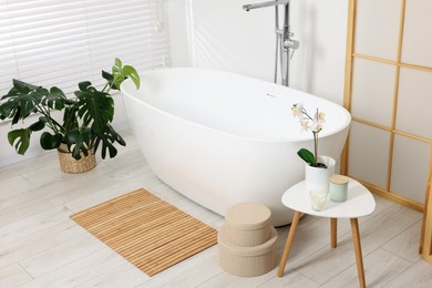 Photo of Stylish bathroom interior with bath tub, houseplants and bamboo mat