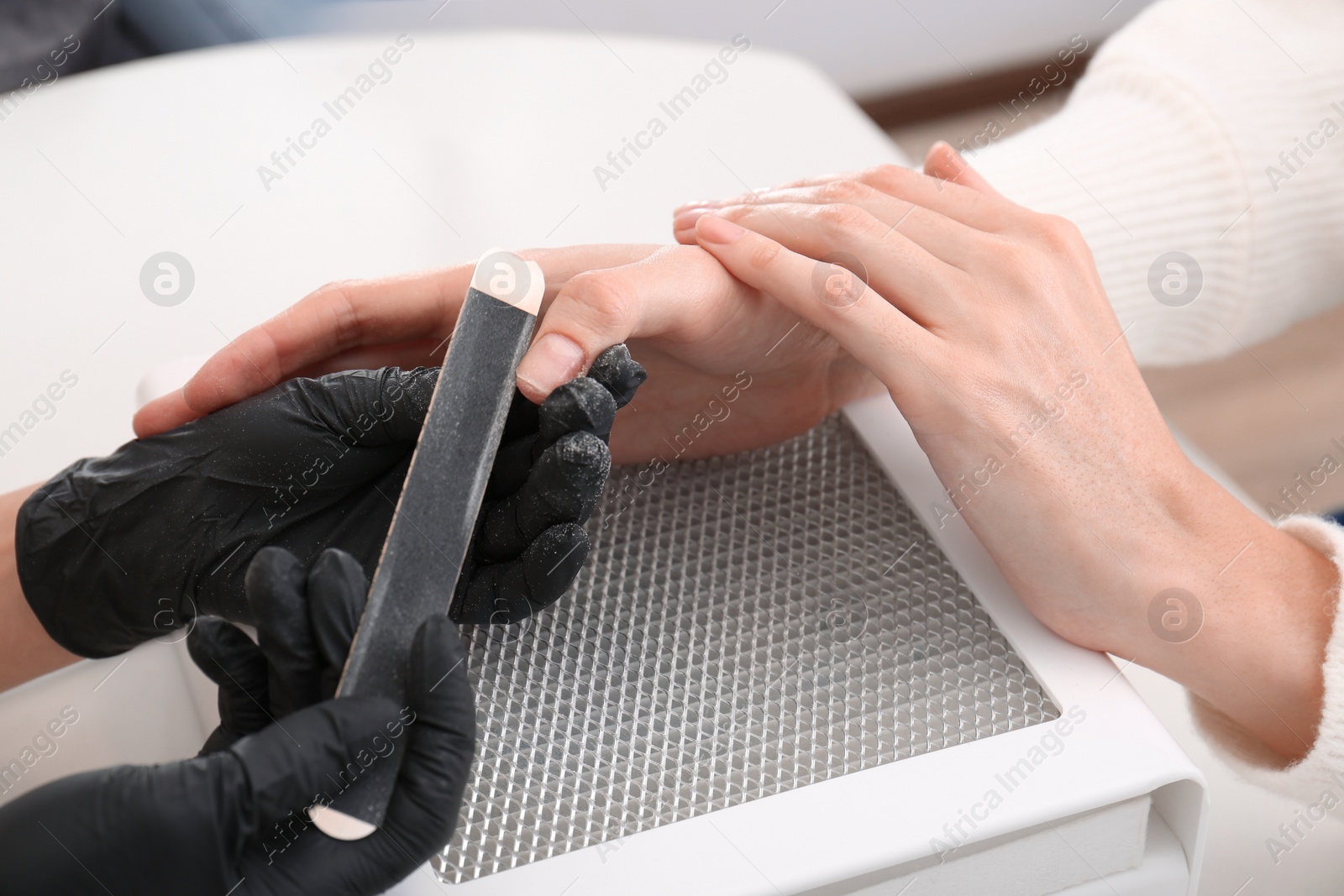 Photo of Professional manicurist working with client at white table, closeup