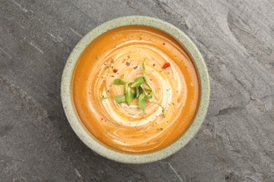 Delicious pumpkin soup with microgreens in bowl on gray table, top view