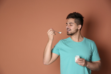 Photo of Happy young man eating tasty yogurt on brown background. Space for text