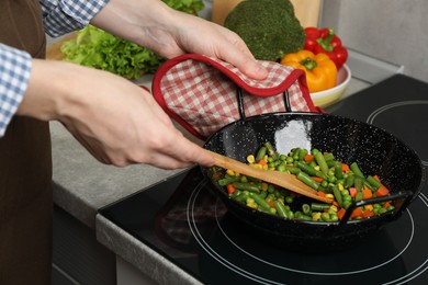 Woman cooking tasty vegetable mix in wok pan at home, closeup