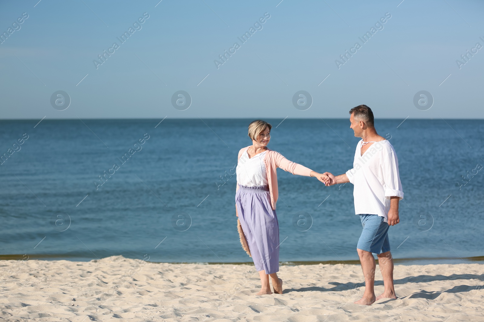 Photo of Happy mature couple holding hands at beach on sunny day