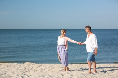 Happy mature couple holding hands at beach on sunny day