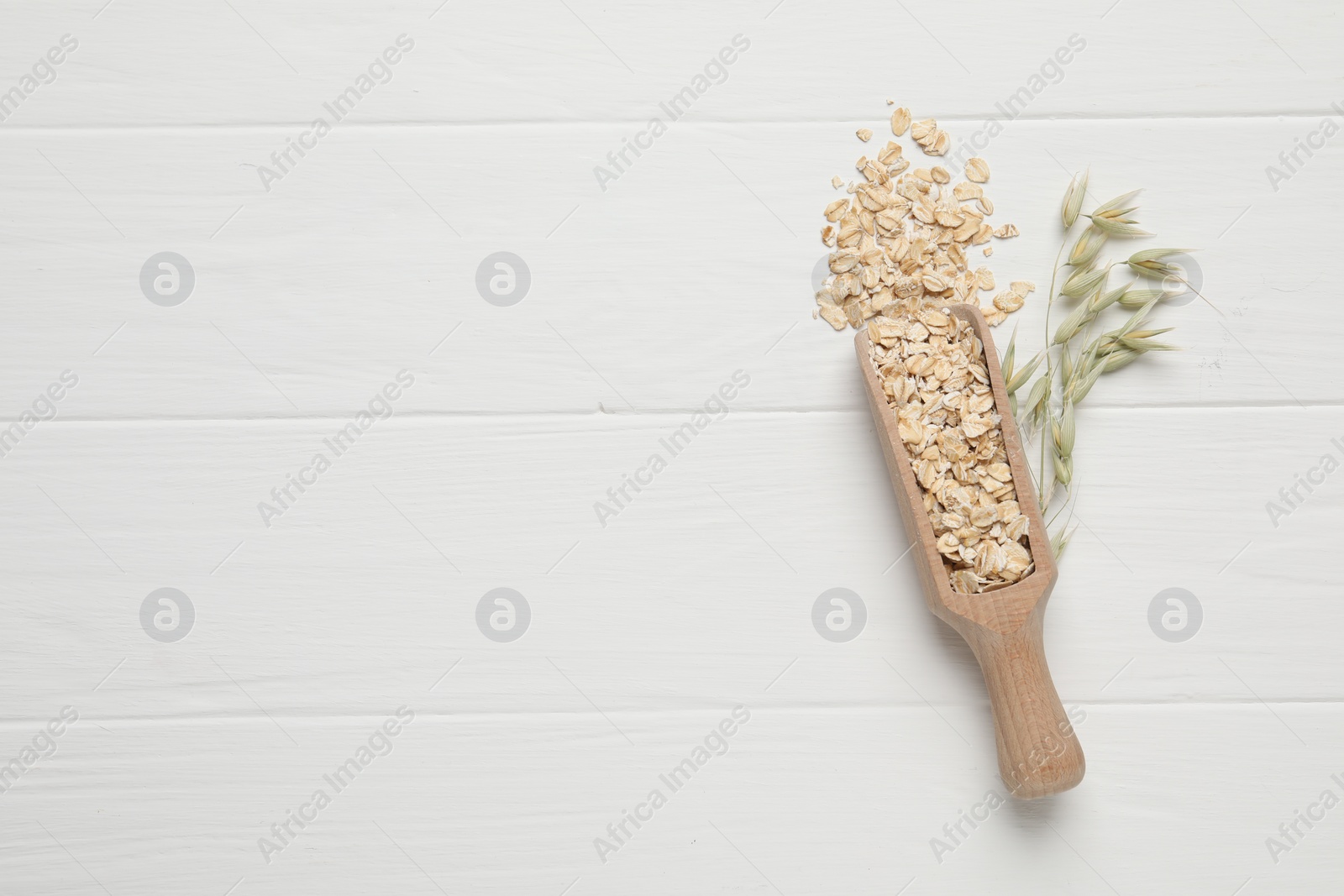 Photo of Scoop with oatmeal and florets on white wooden table, top view. Space for text