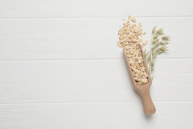 Scoop with oatmeal and florets on white wooden table, top view. Space for text