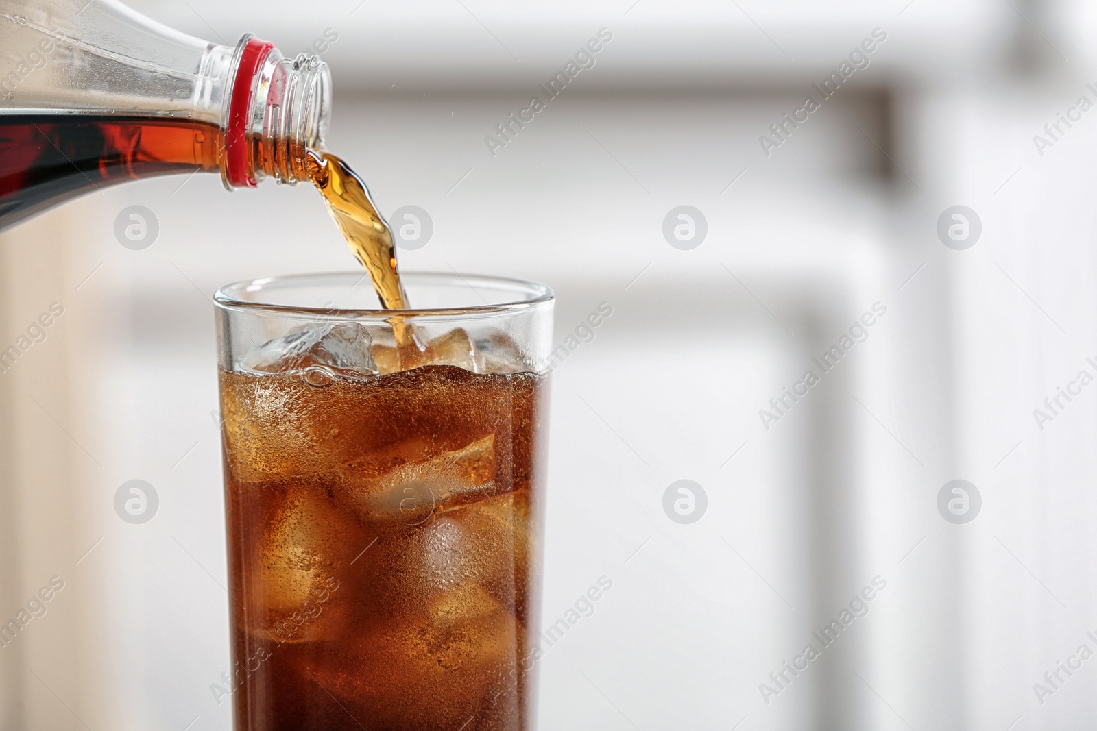 Photo of Pouring cola from bottle into glass on blurred background, closeup. Space for text