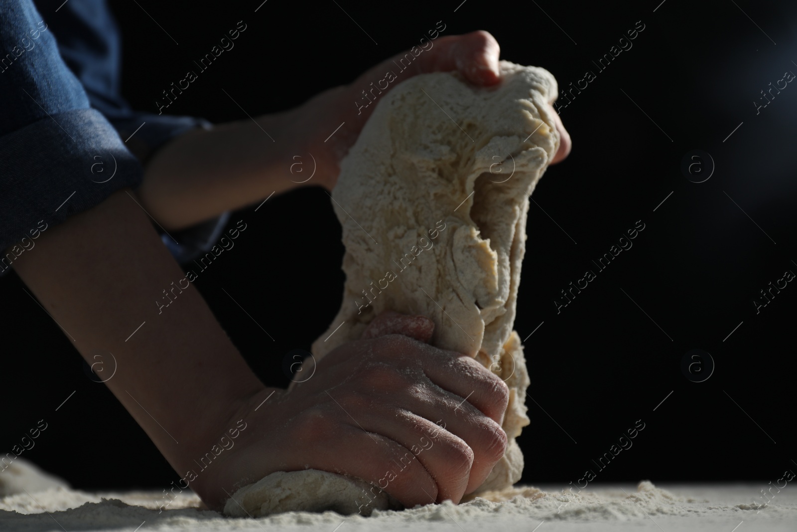 Photo of Making bread. Woman kneading dough at table on dark background, closeup