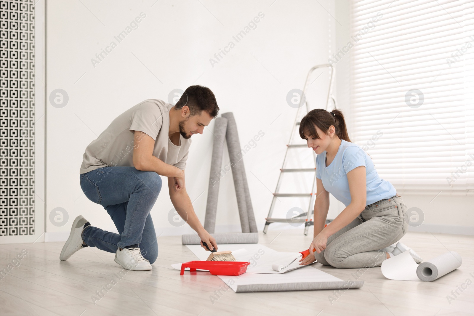 Photo of Couple applying glue onto wallpaper sheet in room