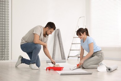 Photo of Couple applying glue onto wallpaper sheet in room