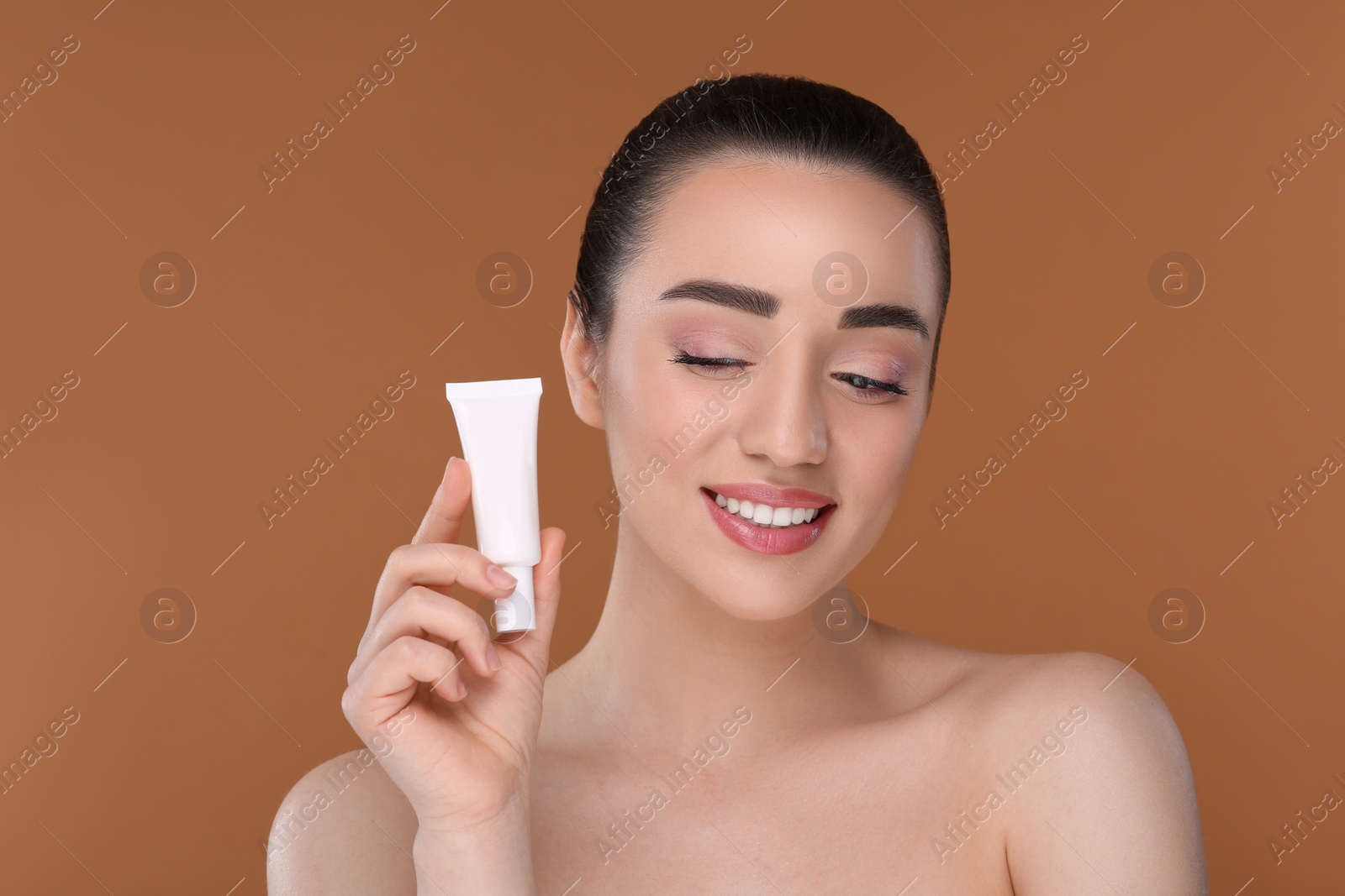 Photo of Woman holding tube of foundation on brown background