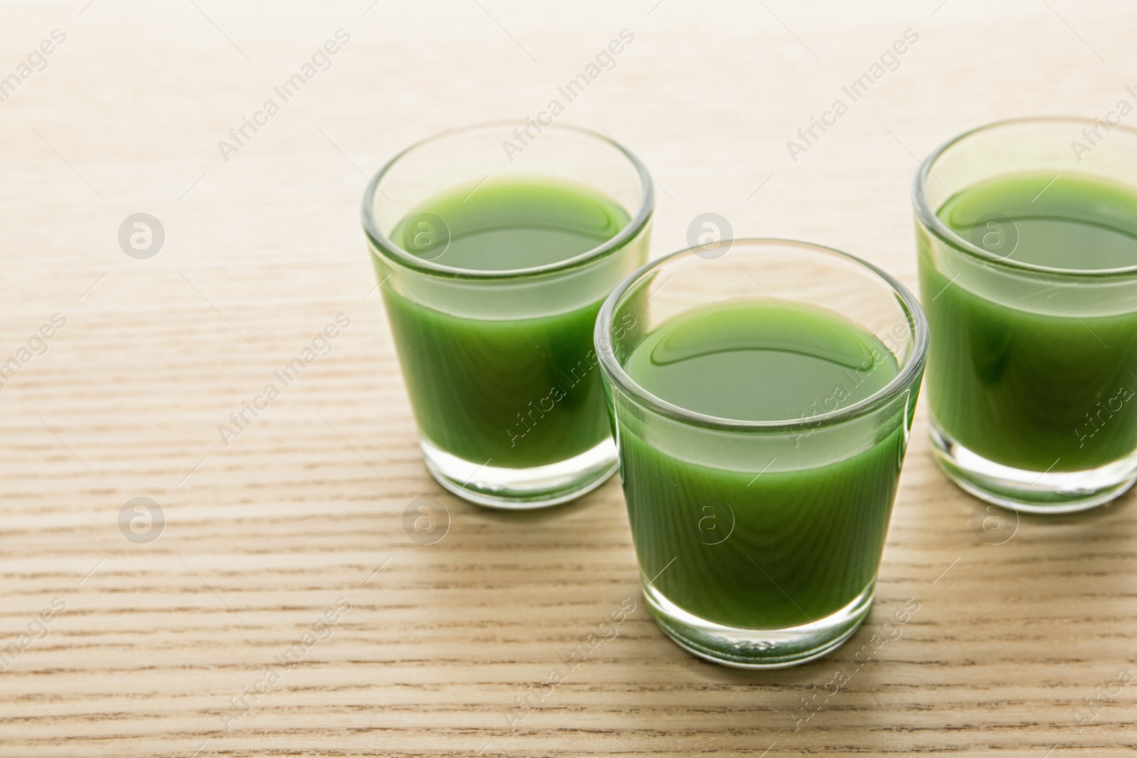 Shot glasses of wheat grass juice on wooden table, space for text Photo of Shot glasses of wheat grass juice on wooden table, space for text