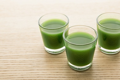 Photo of Shot glasses of wheat grass juice on wooden table, space for text