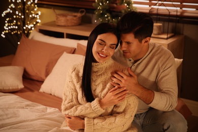 Photo of Happy couple sitting on bed in festively decorated room. Christmas celebration