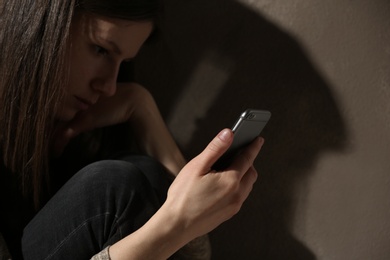 Sad woman with smartphone in dark room. Loneliness concept