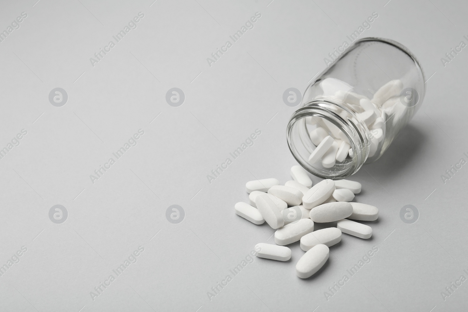 Photo of Vitamin pills and bottle on grey background, closeup. Space for text