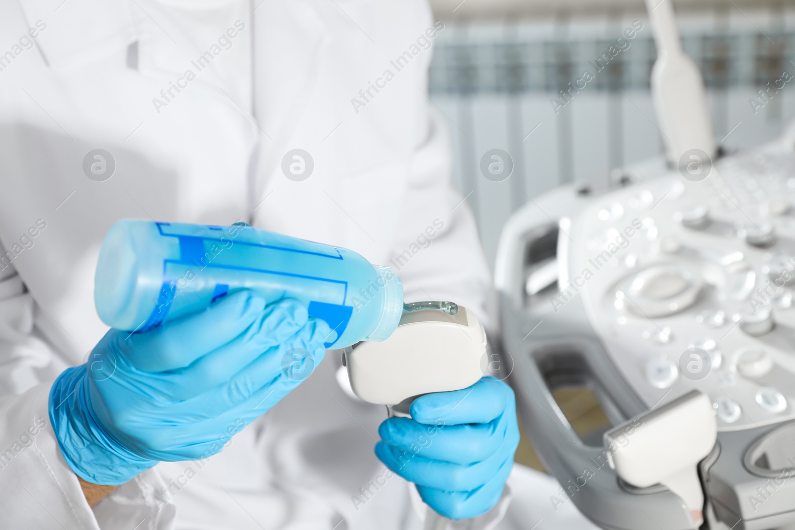 Photo of Sonographer covering ultrasound machine probe with gel in clinic, closeup