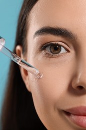 Photo of Beautiful young woman applying serum onto her face on light blue background, closeup