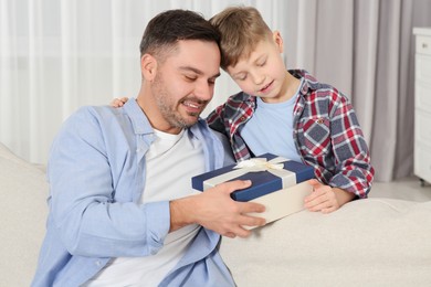 Photo of Cute little boy presenting his father with gift on sofa at home