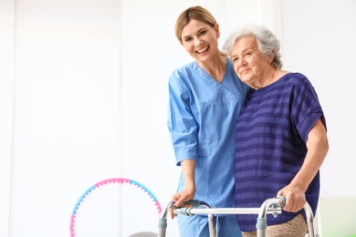 Photo of Caretaker helping elderly woman with walking frame indoors