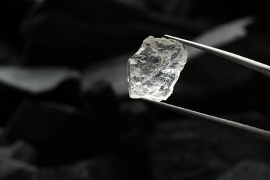 Tweezers with shiny rough diamond on dark background, closeup