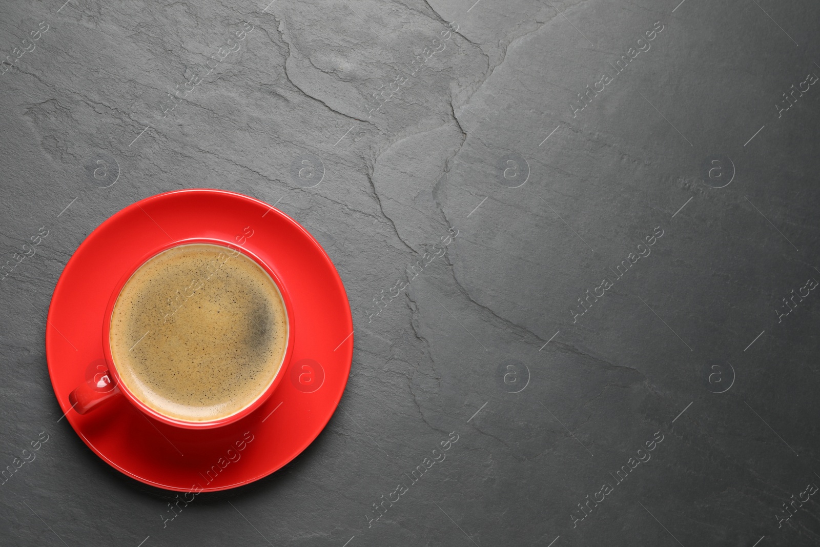 Photo of Aromatic coffee in red cup on black background, top view. Space for text