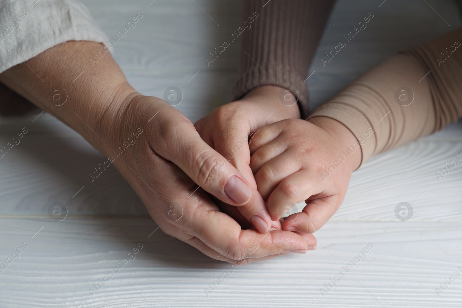 Photo of Family holding hands together at white wooden table, closeup