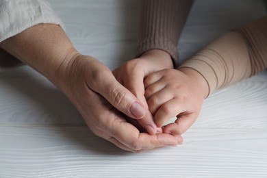 Photo of Family holding hands together at white wooden table, closeup