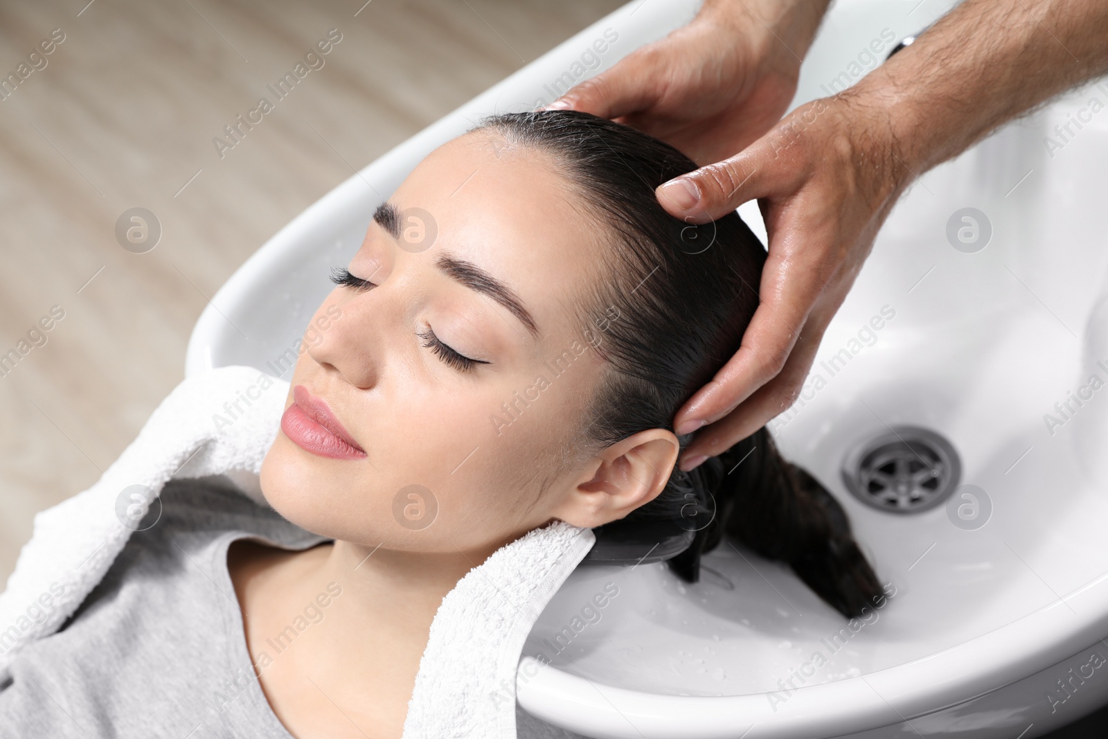 Photo of Stylist washing client's hair at sink in beauty salon