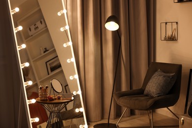 Photo of Makeup room. Stylish mirror with light bulbs, beauty products on table and armchair indoors