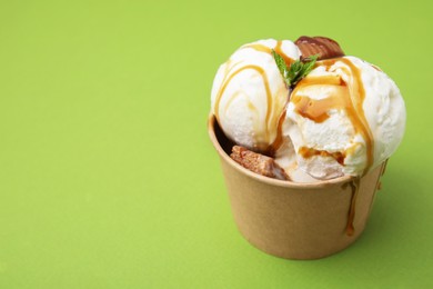 Photo of Scoops of tasty ice cream with mint, caramel sauce and candies in paper cup on green background. Space for text