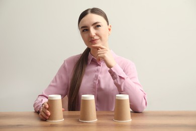 Photo of Thoughtful woman playing shell game at wooden table