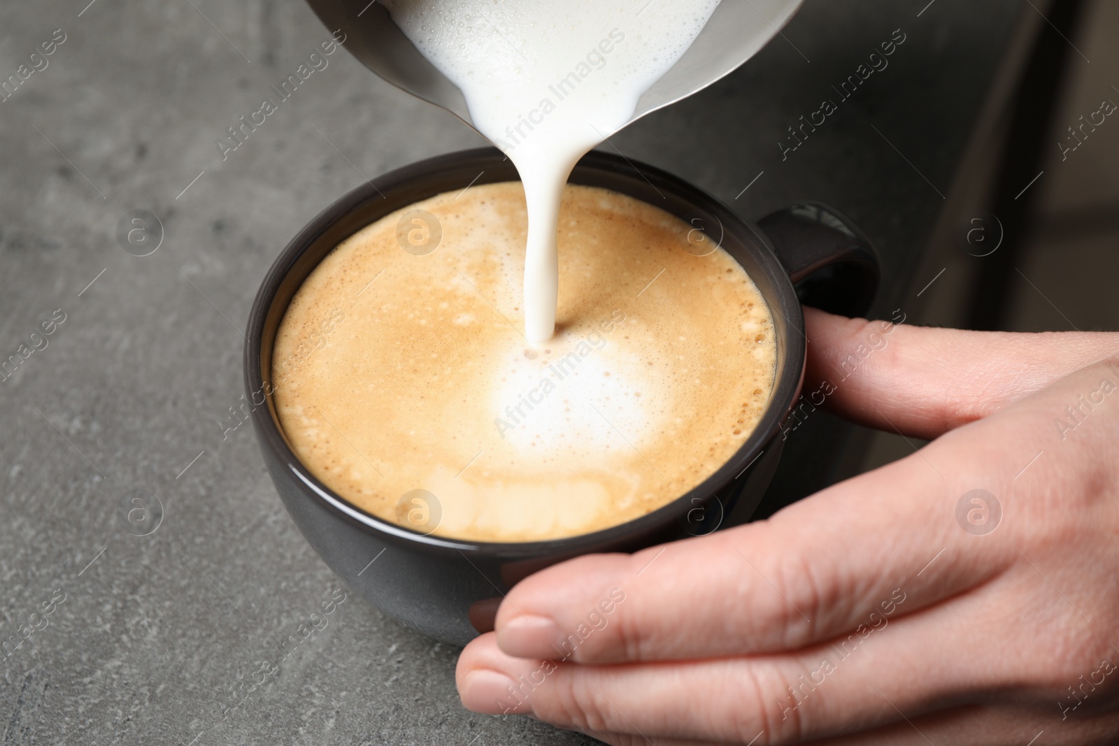 Photo of Woman pouring milk into cup of coffee at grey table, closeup